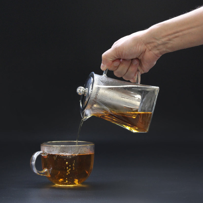 Hand pouring tea from a glass teapot with drip-free spout into a glass cup - Kraas