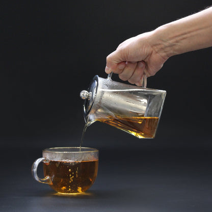 Hand pouring tea from a glass teapot with drip-free spout into a glass cup - Kraas