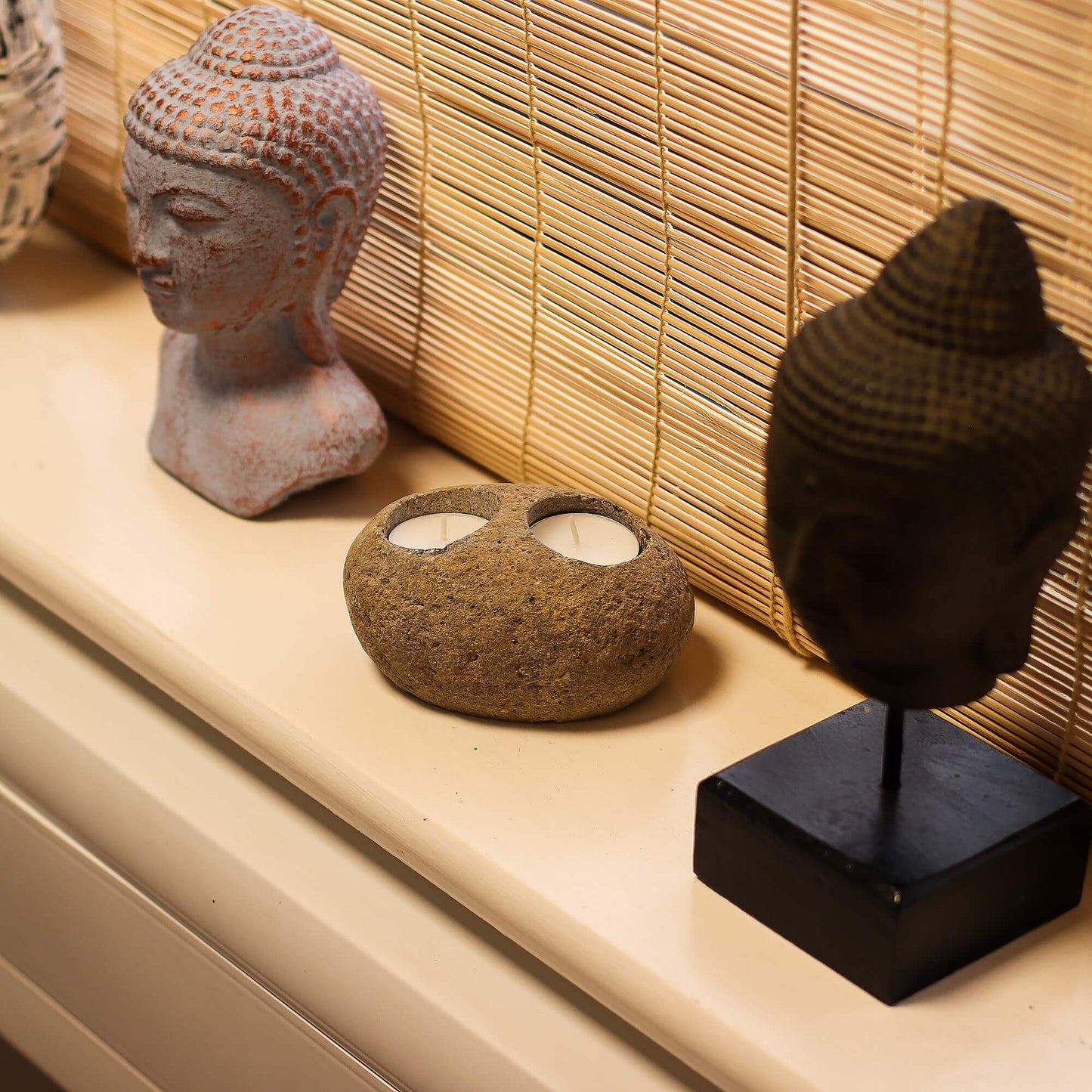 River stone candle holder placed on a shelf with a stone Buddha head and black Buddha head statue - Kraas