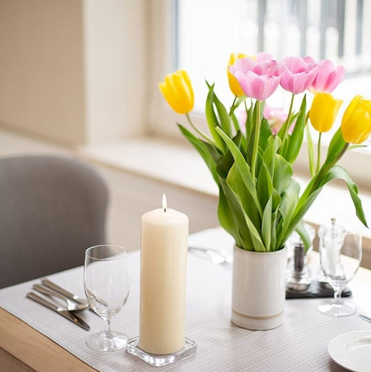 Table setting with tulips in a vase, ivory pillar candle, and glasses - Kraas