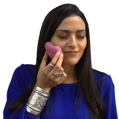 Woman applying soft pink konjac sponge to face for skincare cleansing and hydration - Kraas